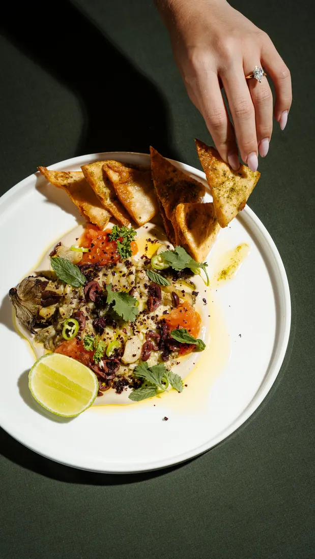 Creamy eggplant dip with fried pita, a hand reaching for a chip