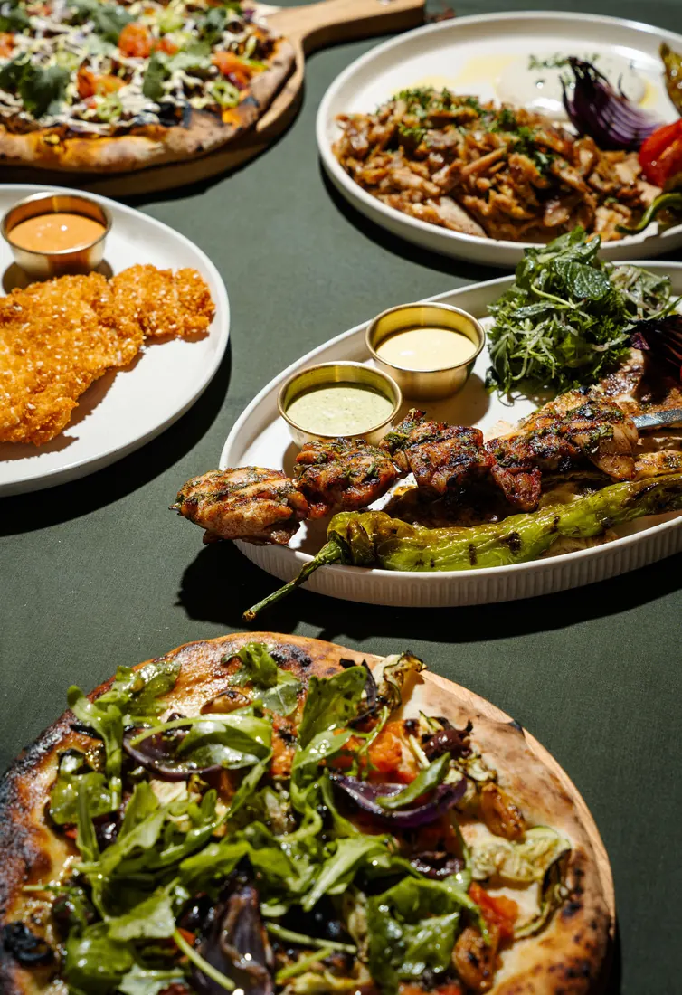 Table spread of flatbreads, schnitzel and skewers on green linen
